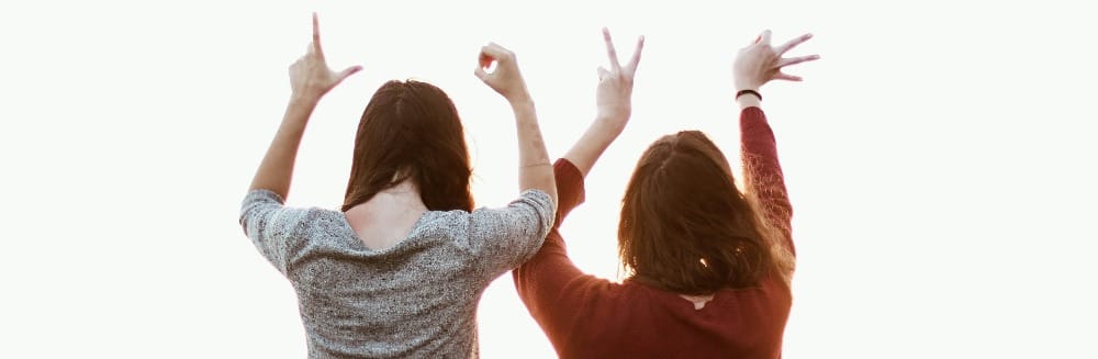 two women sitting while making love hand sign at daytime