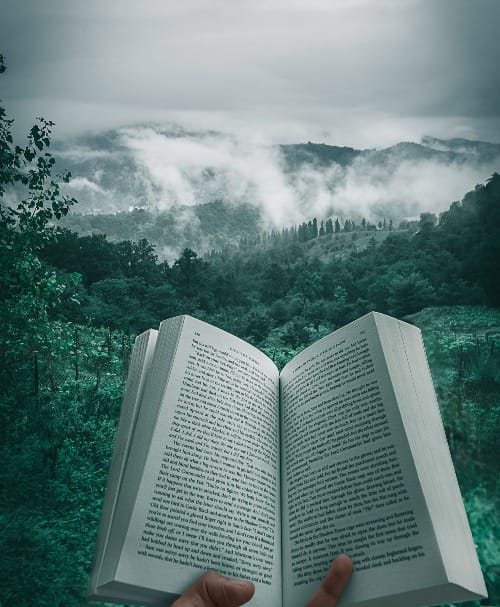 person holding open book viewing mountain view