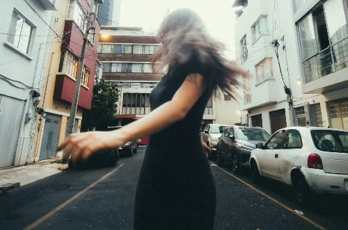 Woman in black dress twirling on city street